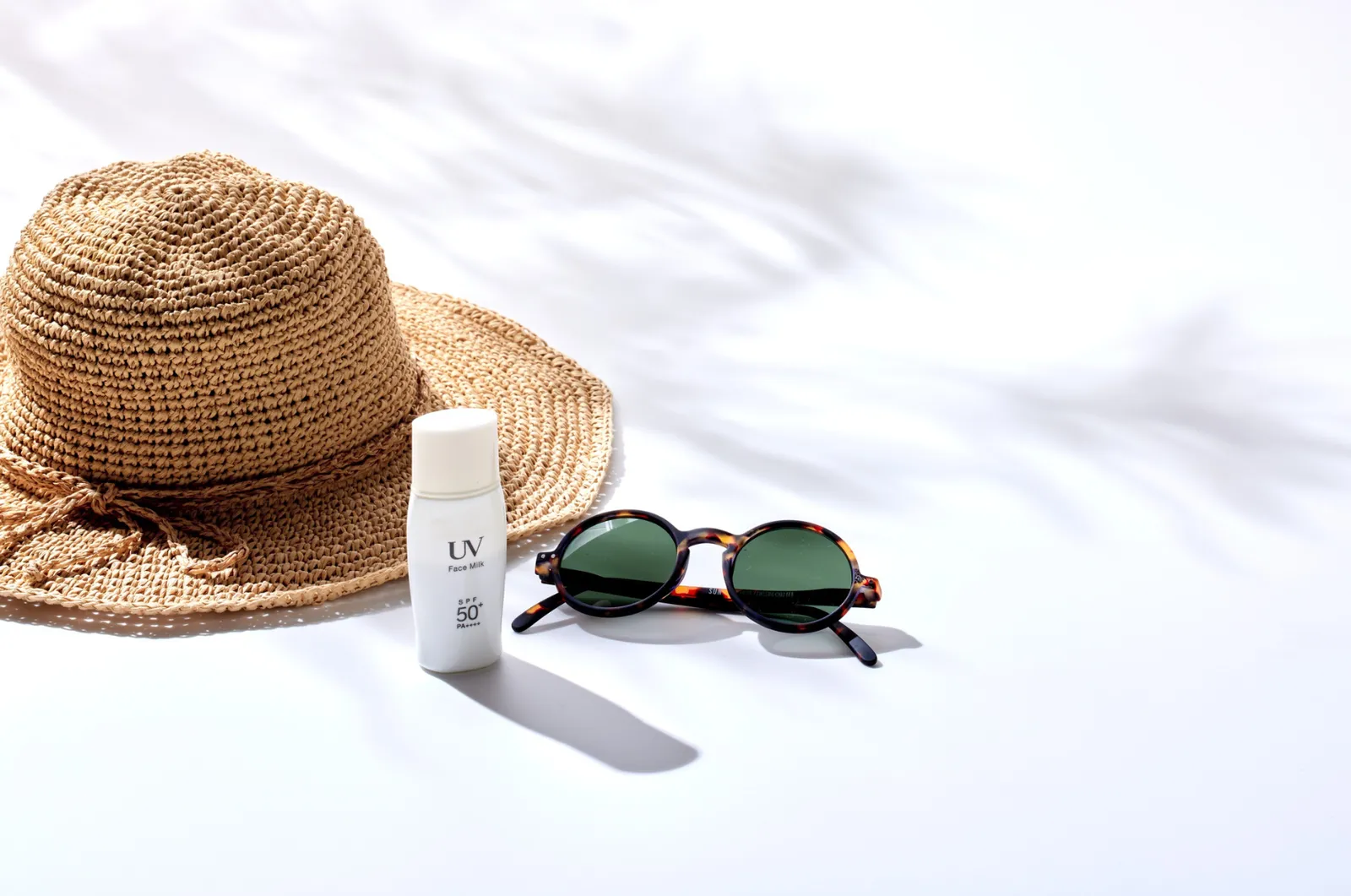 Strohhut, Sonnencreme und Sonnenbrille in praller Sonne, darüber der Schatten von Palmblättern
